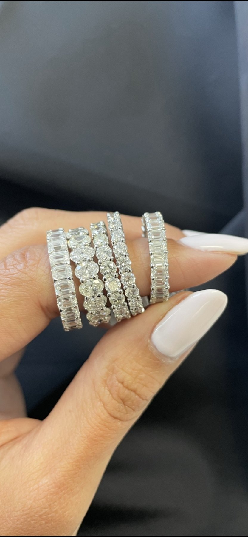 Five diamond eternity bands with emerald, oval, round and baguette diamonds held in hand