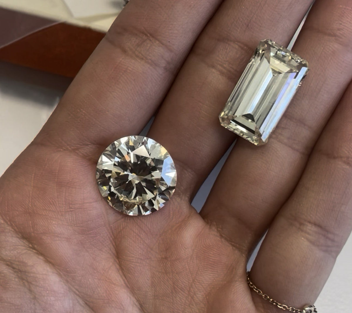 Loose emerald cut diamond next to a round brilliant diamond in the palm of a hand, showing the open step-cut facets