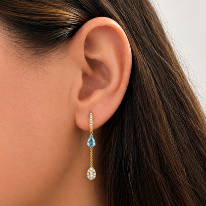 Detail of suspended blue topaz drop and pave diamonds on 18k yellow gold mini hoop